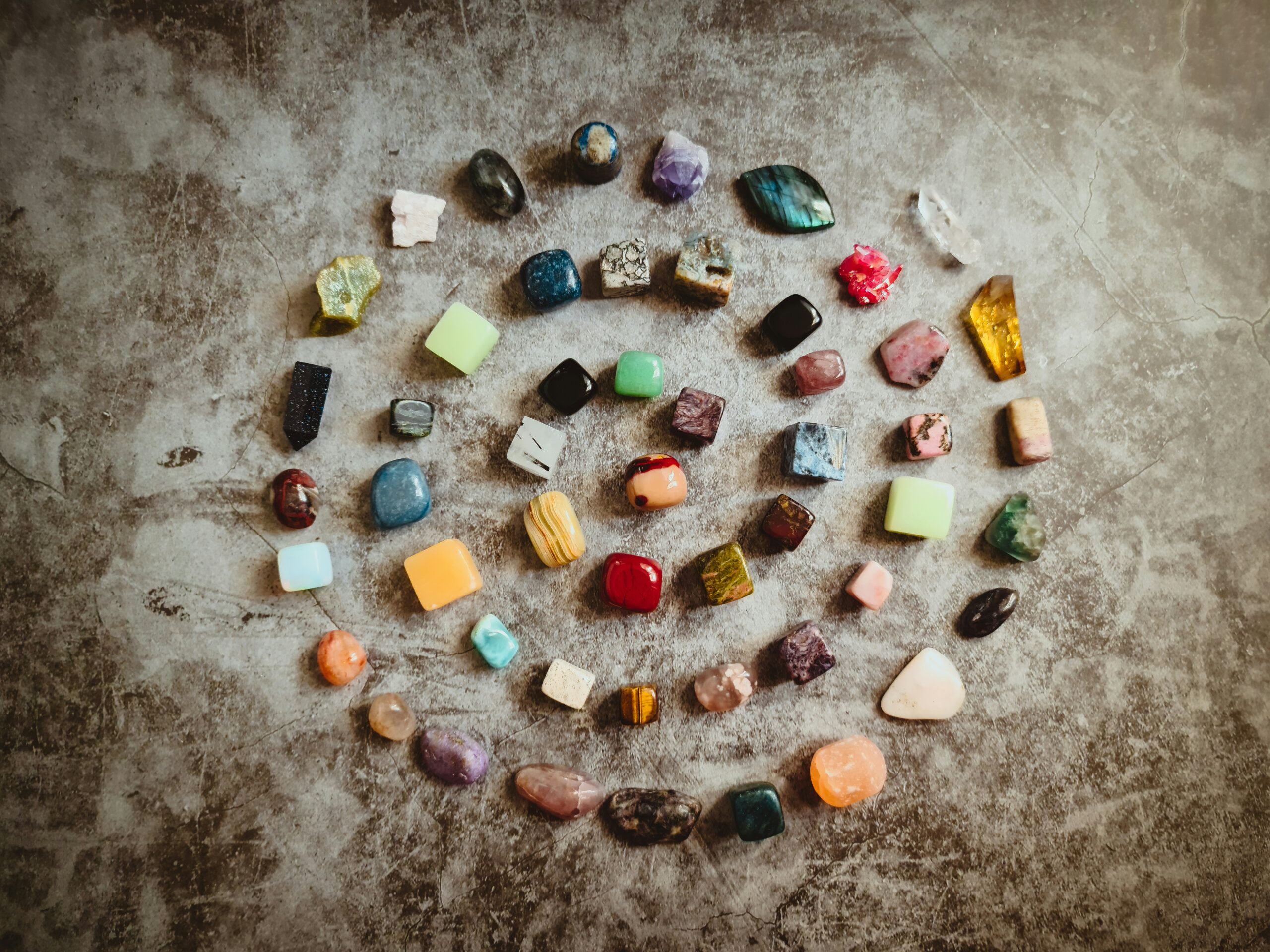Colorful gemstones laid out in a spiral on a grey concrete floor