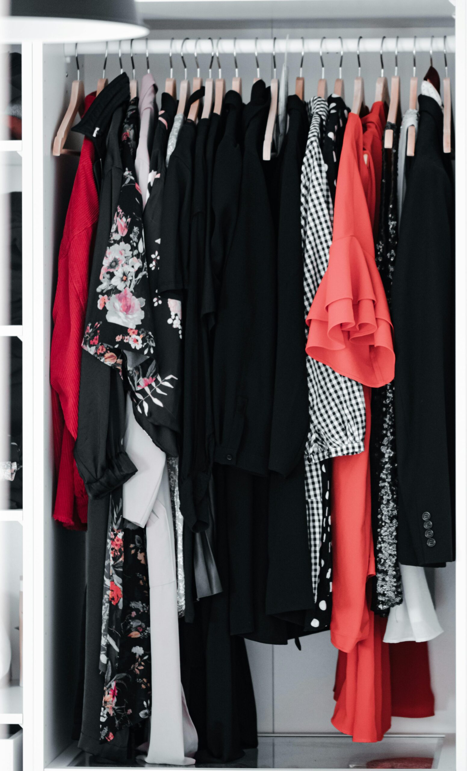 A clothing rack in a closet with various dresses and shirts in red, black, and white colors and patterns.