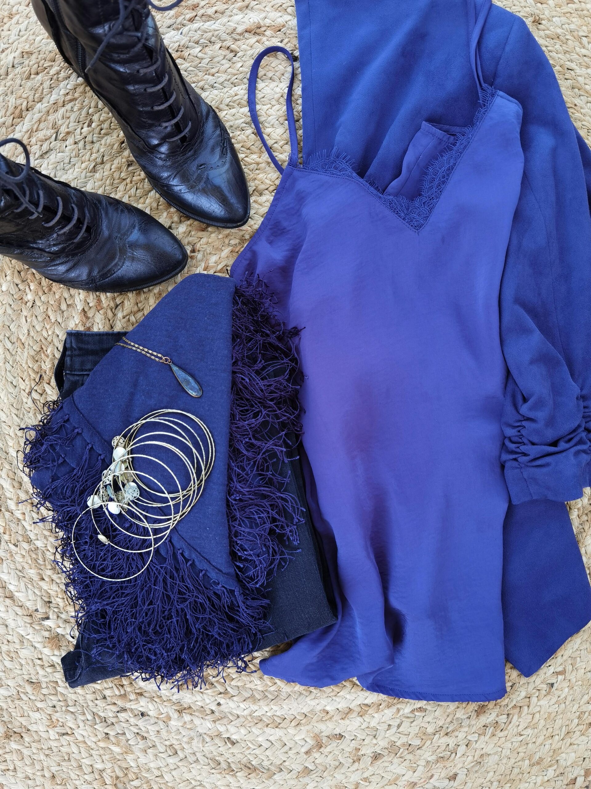 A flat lay of a blue monochrome outfit with jeans, a silk top, boots, and accessories