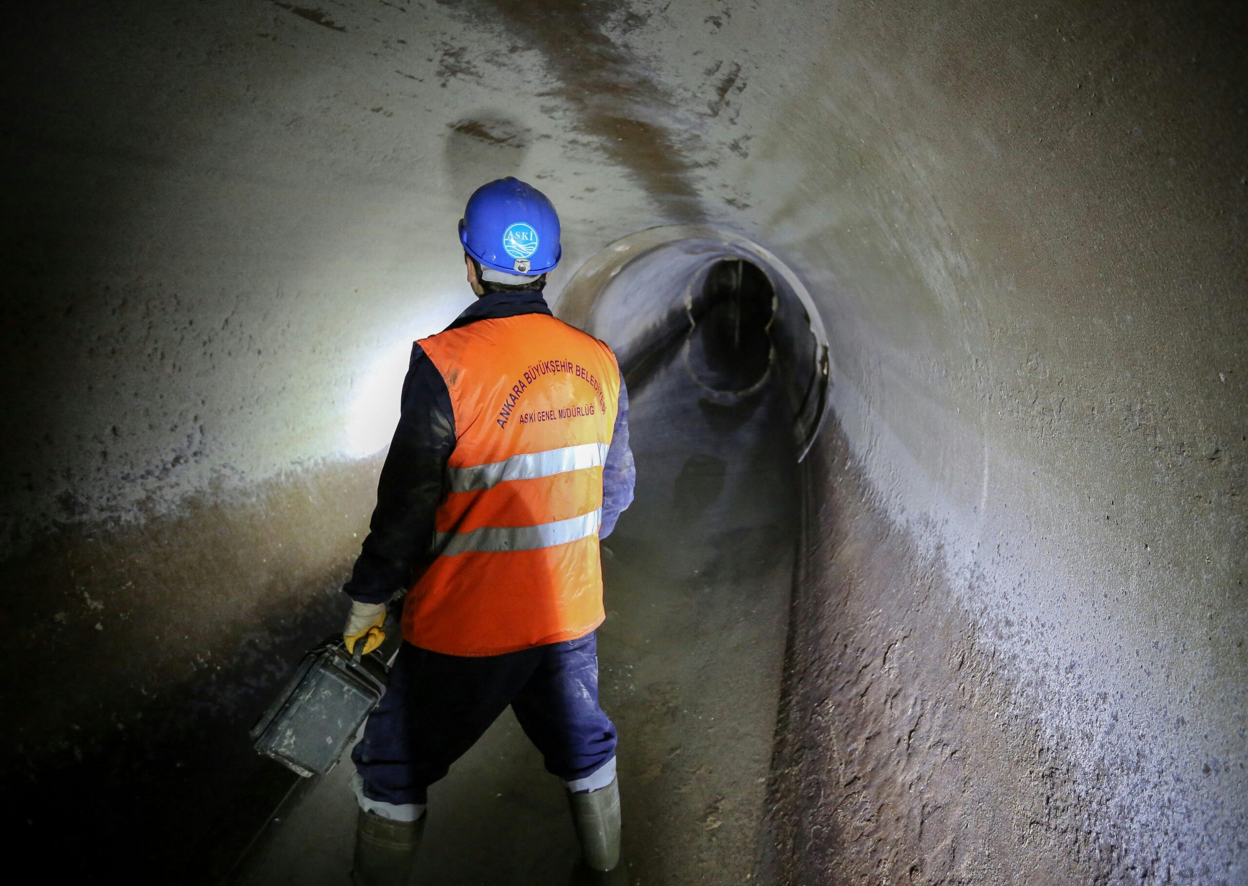 A worker wearing a reflective orange vest and a blue helmet in a sewer