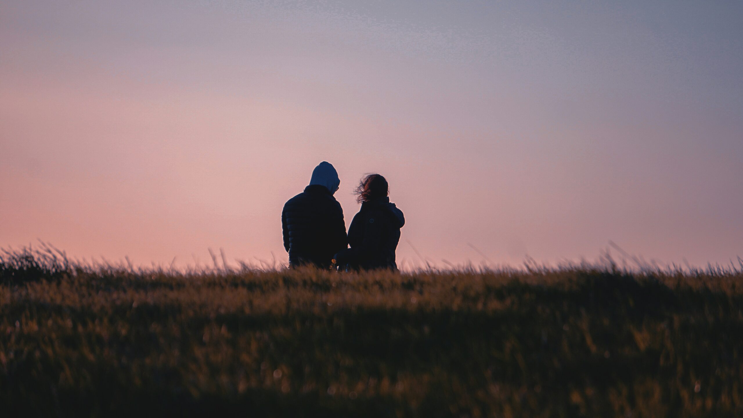 A couple sitting on the grass with a pink sunset in the background