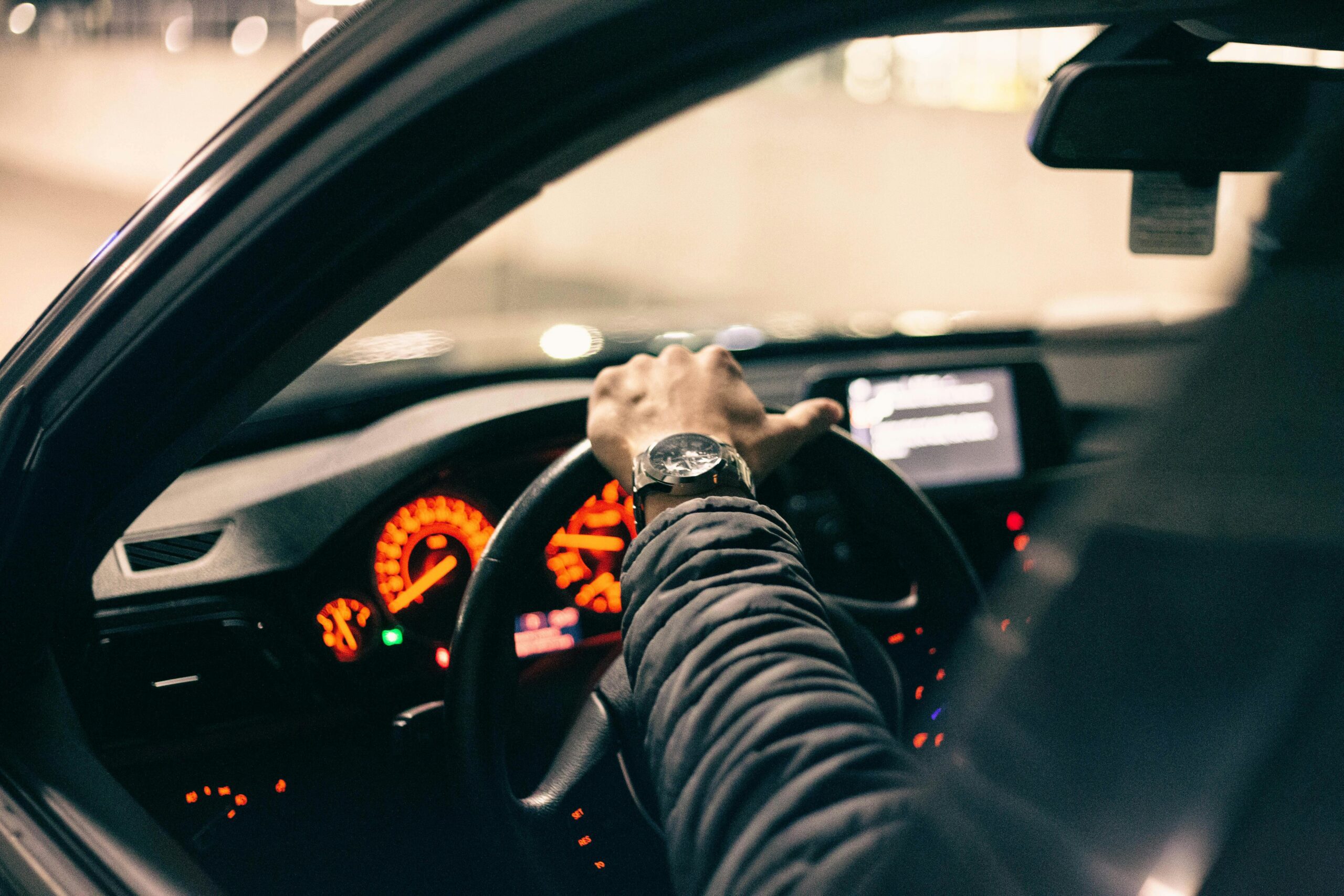 A close up of a person driving a car and wearing a jacket and watch