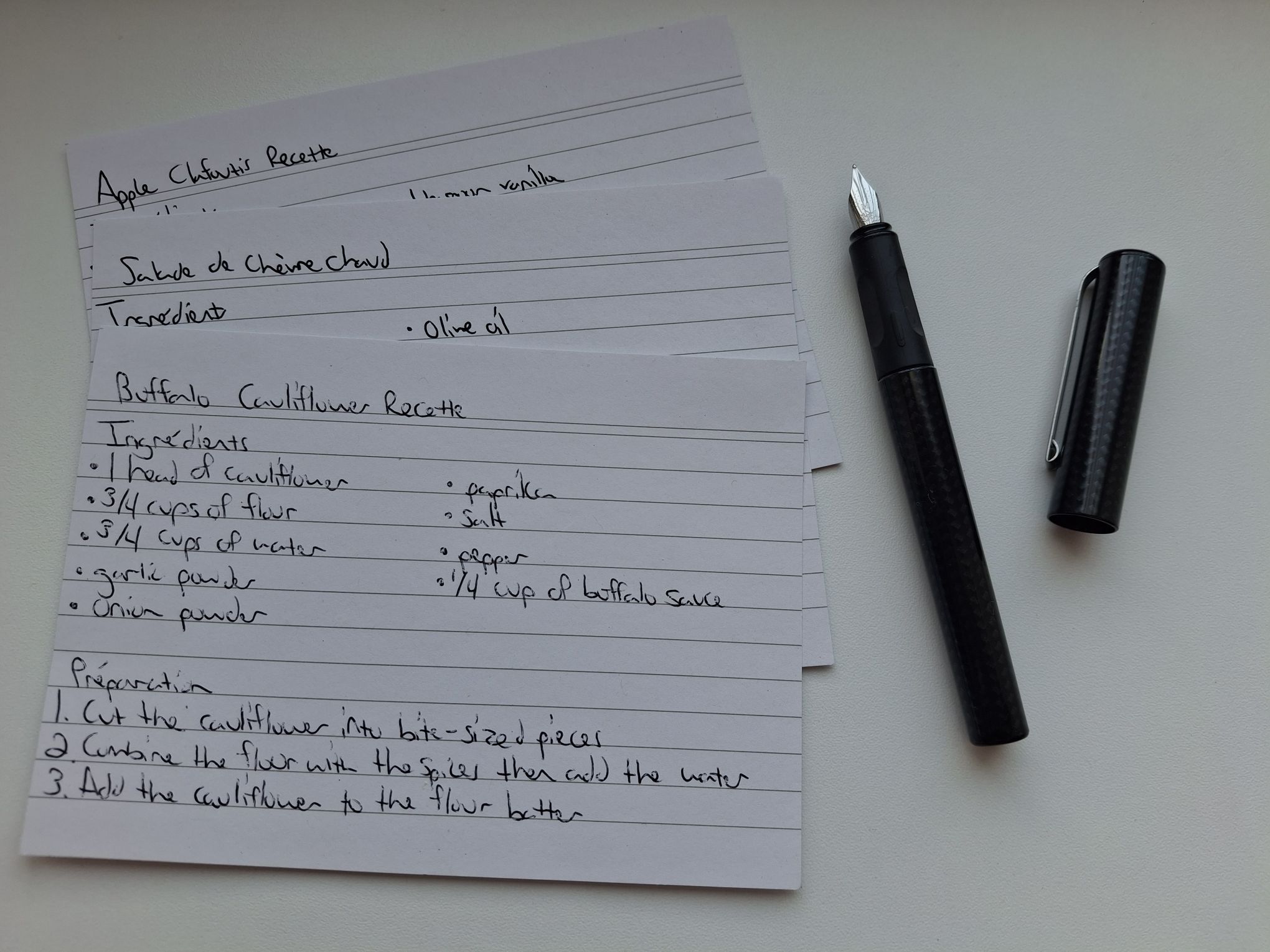 The handwritten recipe cards for buffalo cauliflower, salade de chèvre chaud, and apple clafoutis next to a fountain pen