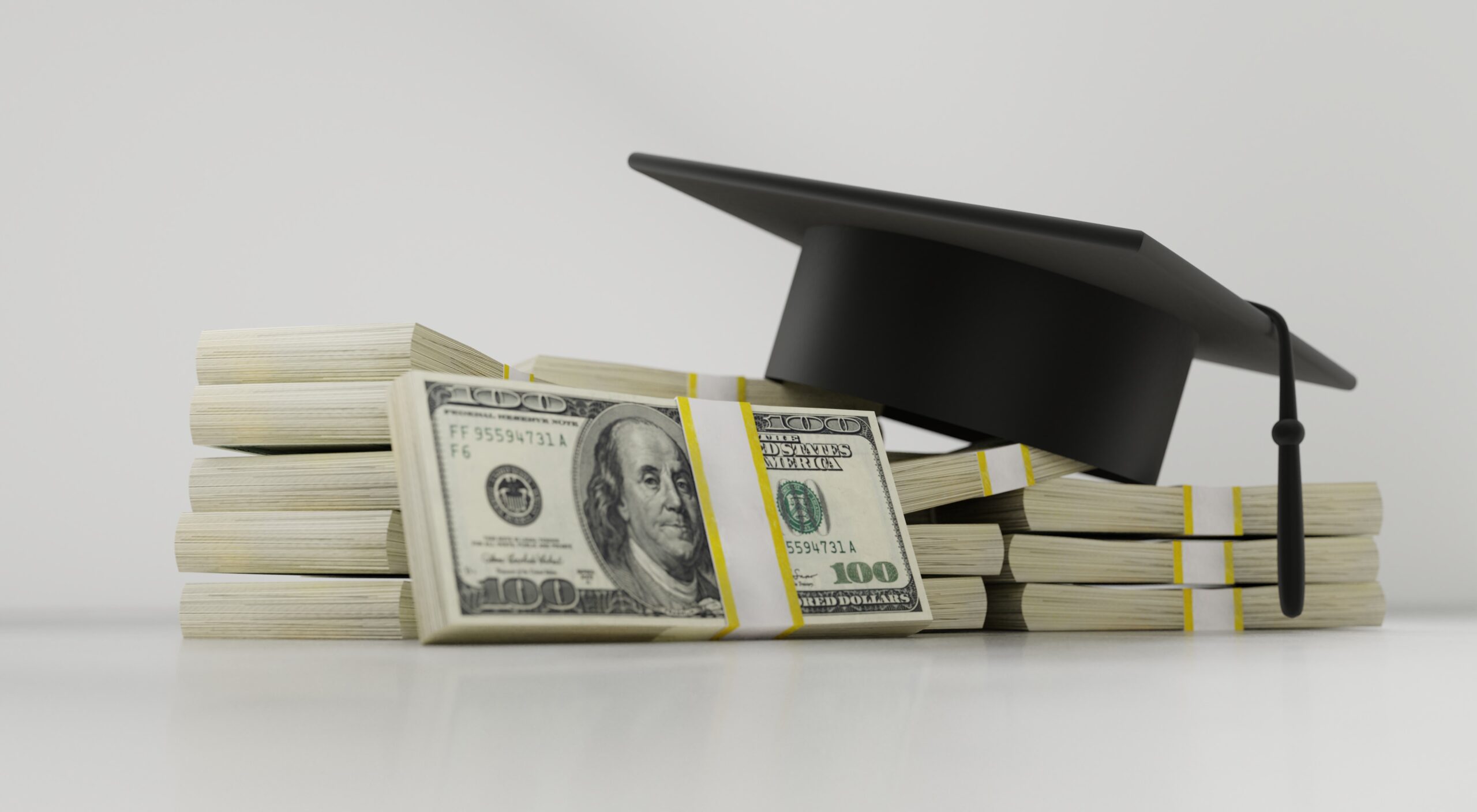 A black graduation cap next to bundles of 100 dollar bills. 