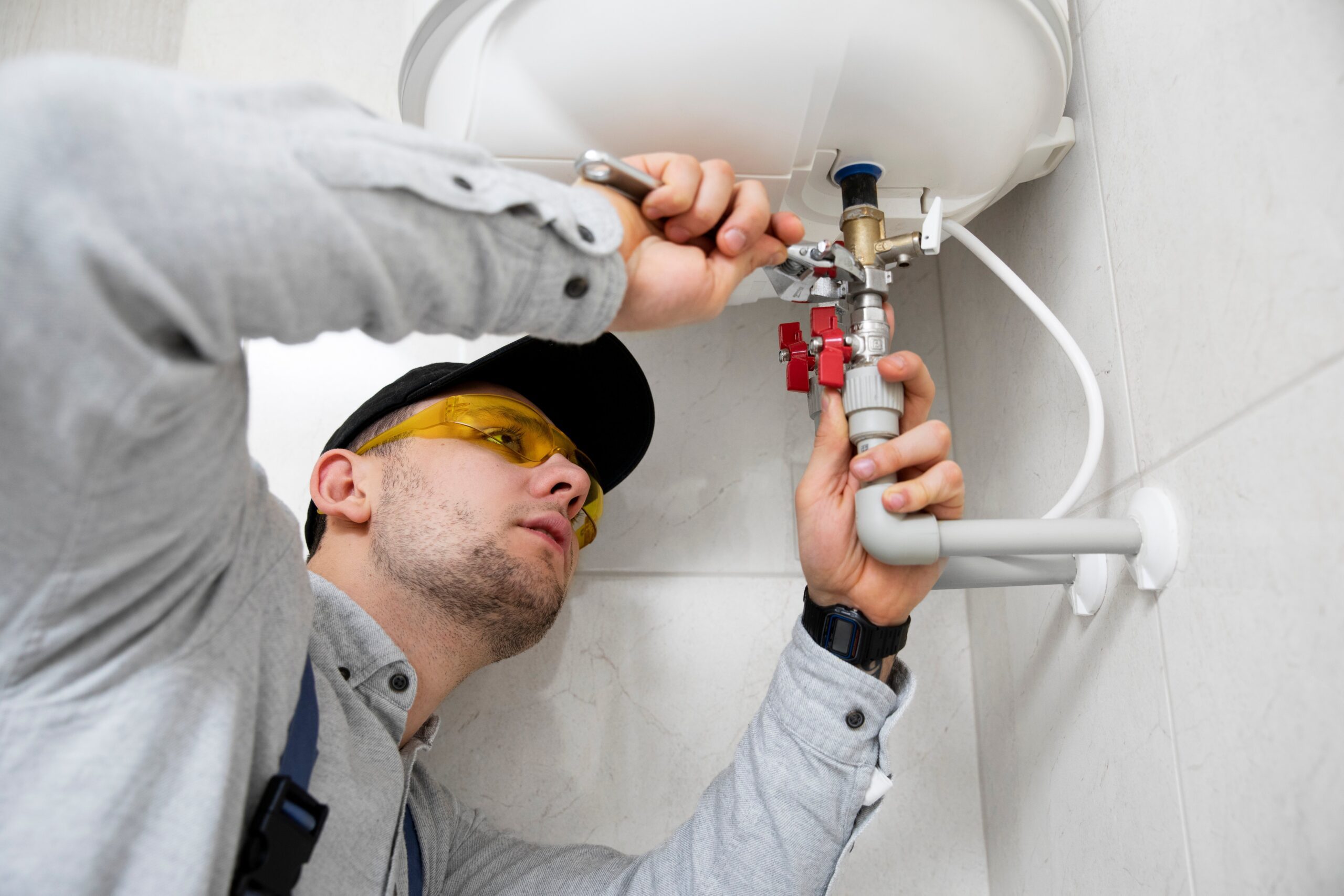 A professional plumber wearing safety glasses and fixing the pipes to a sink