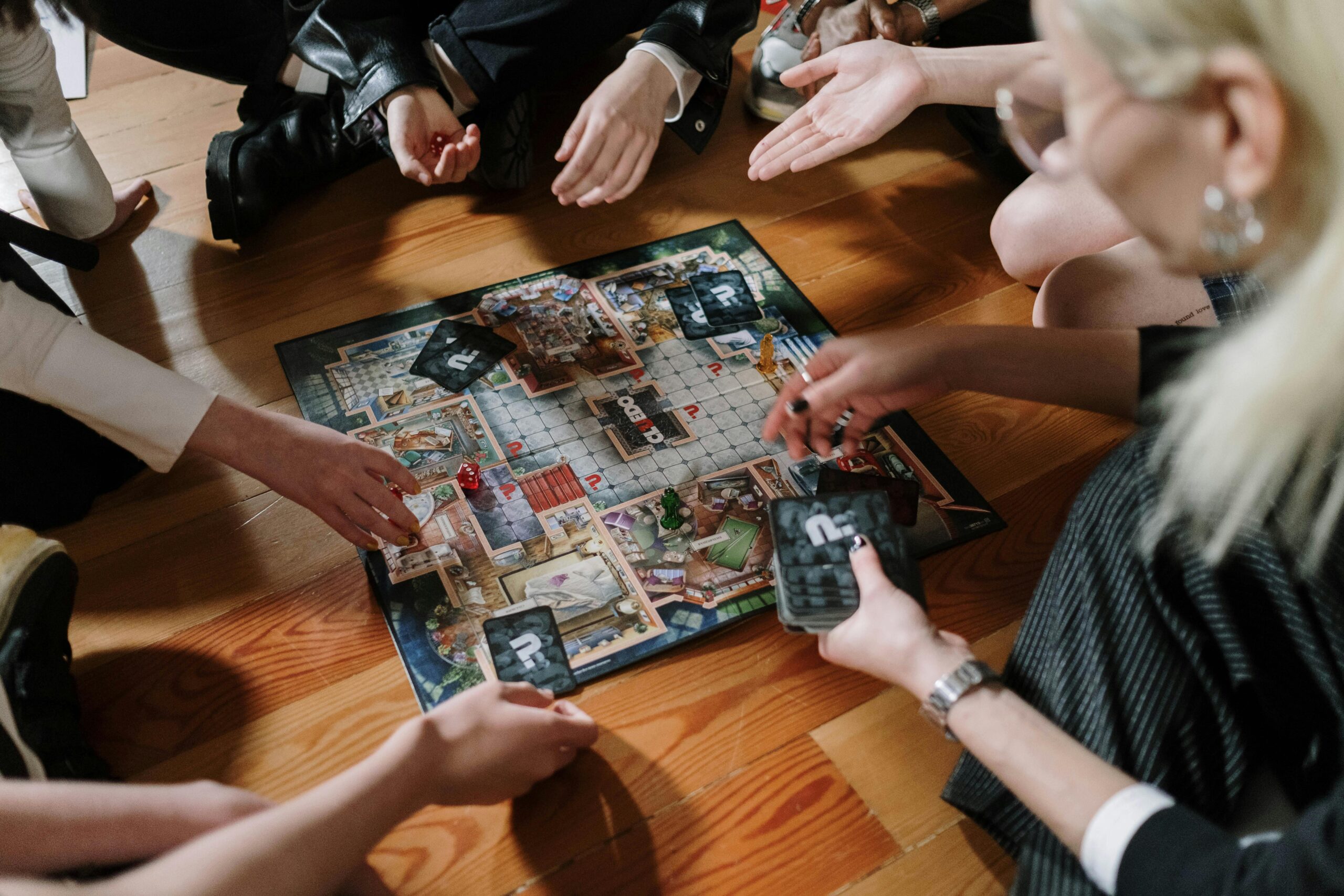 A group of people gathering around the board game Clue (Cluedo)