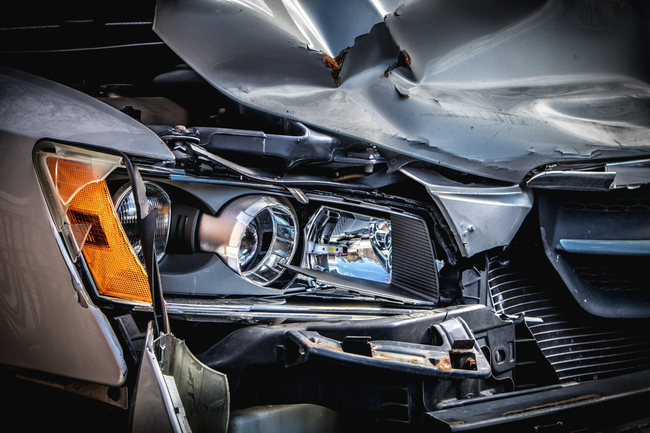 A close-up of a car with damage to the front of the vehicle including the headlight and hood