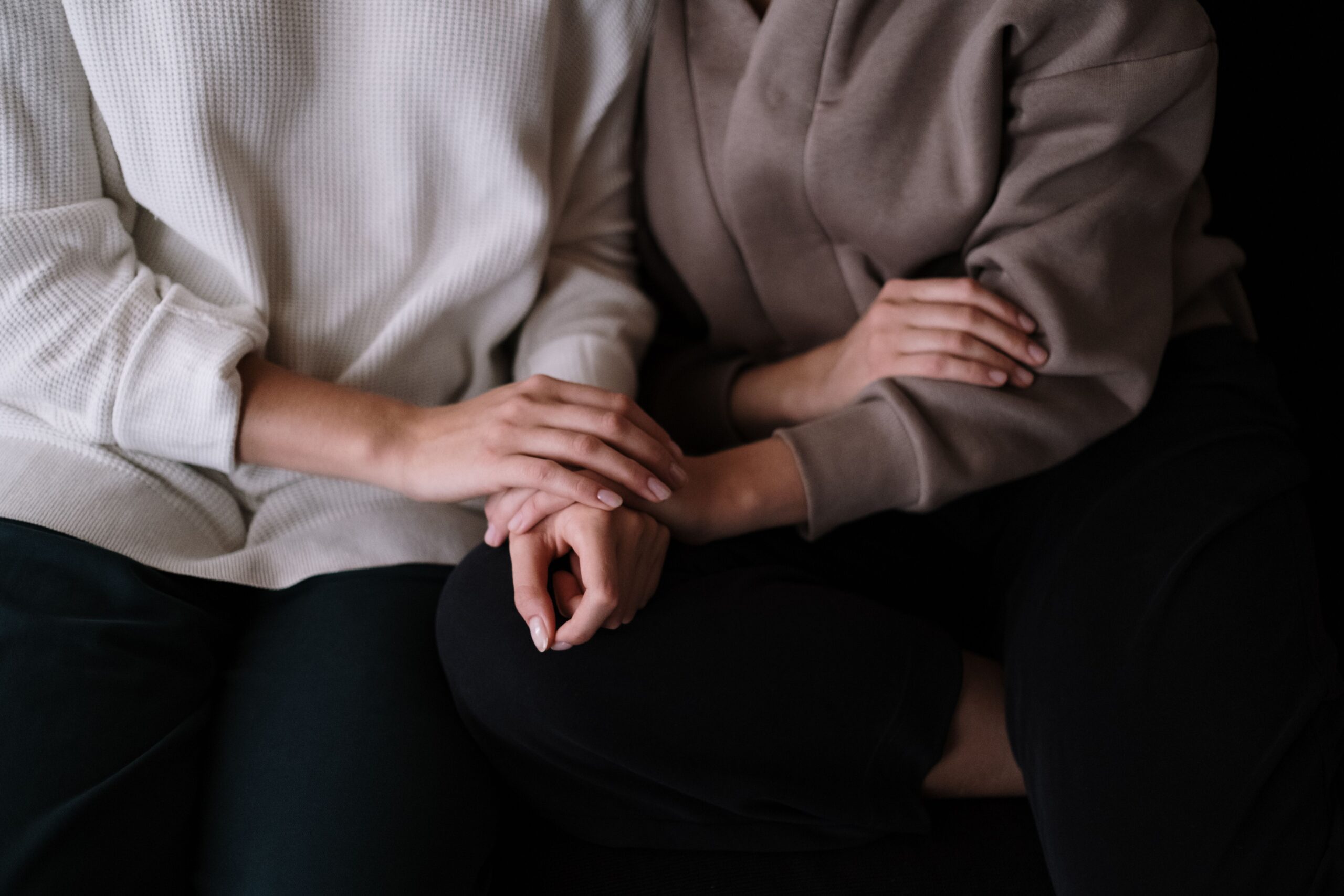 A closeup of two individuals sitting next to each other. One person has their hand over the person's hand, providing comfort and support with gentle touch.