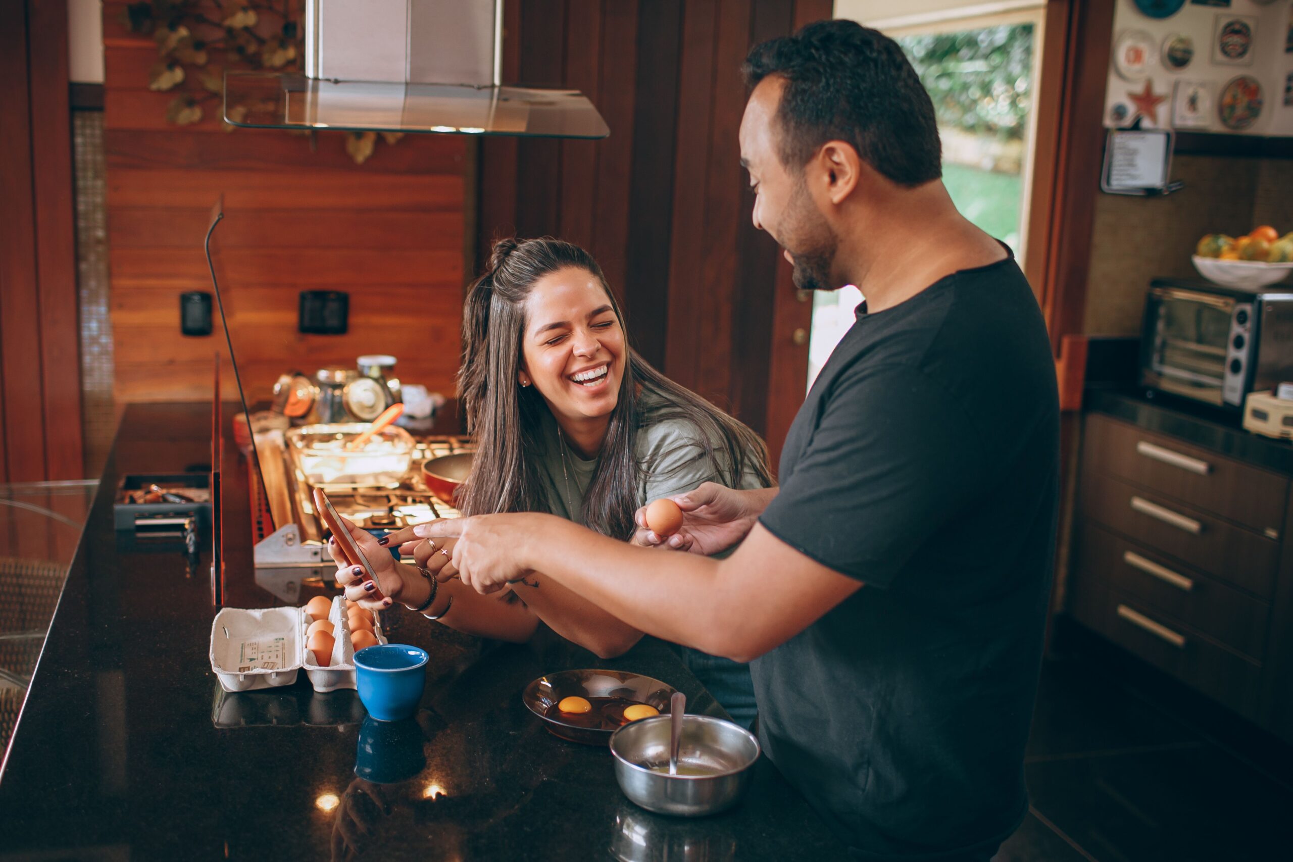 A couple smiling and laughing while in the kitchen and making a meal together