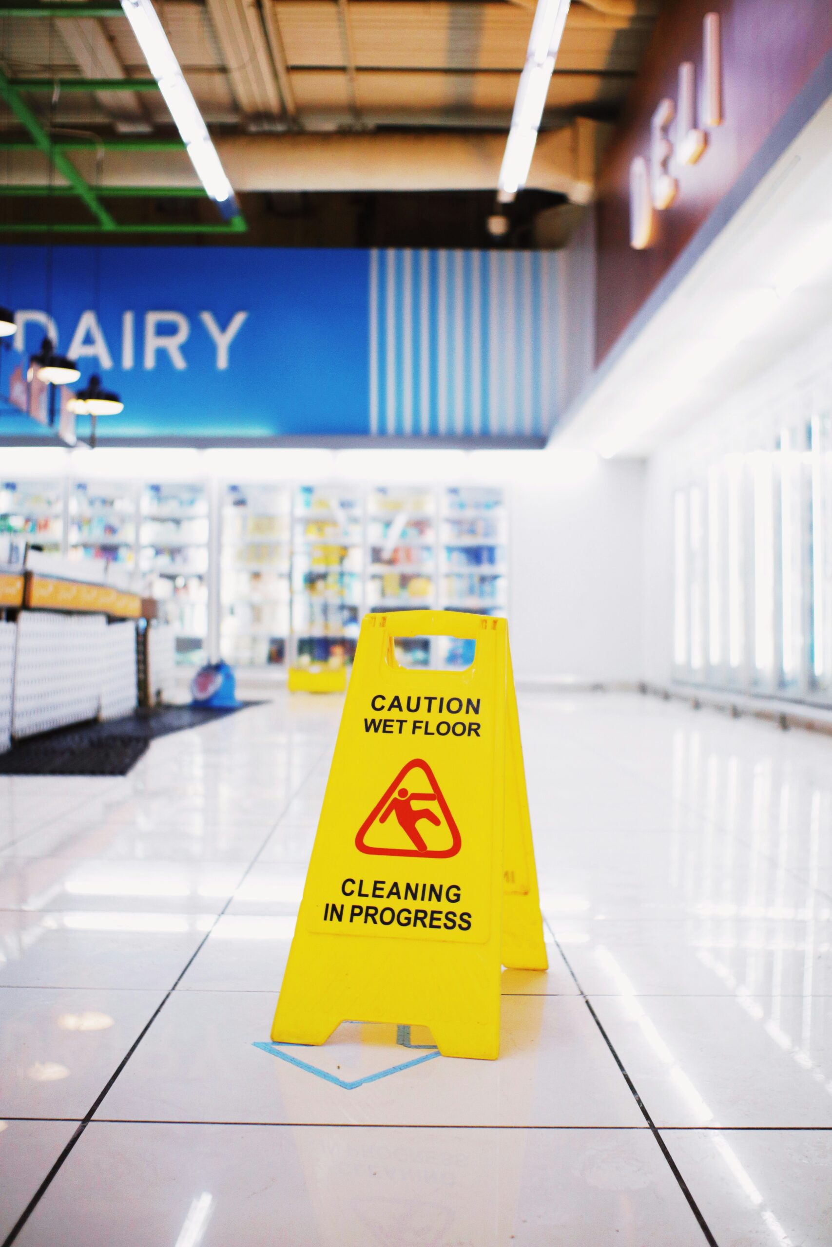 A yellow "caution wet floor cleaning in progress" sign in an aisle of a grocery store