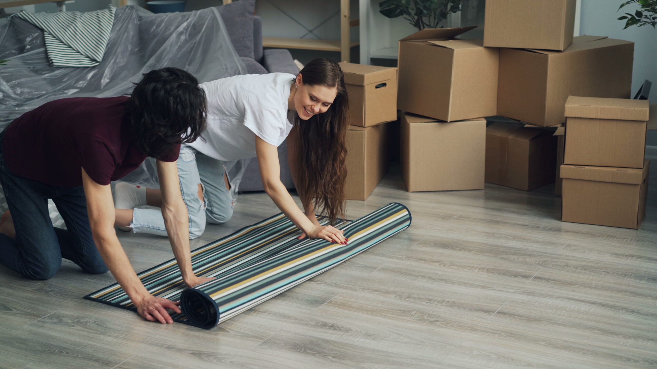 A man and woman putting a striped rug on a wooden floor